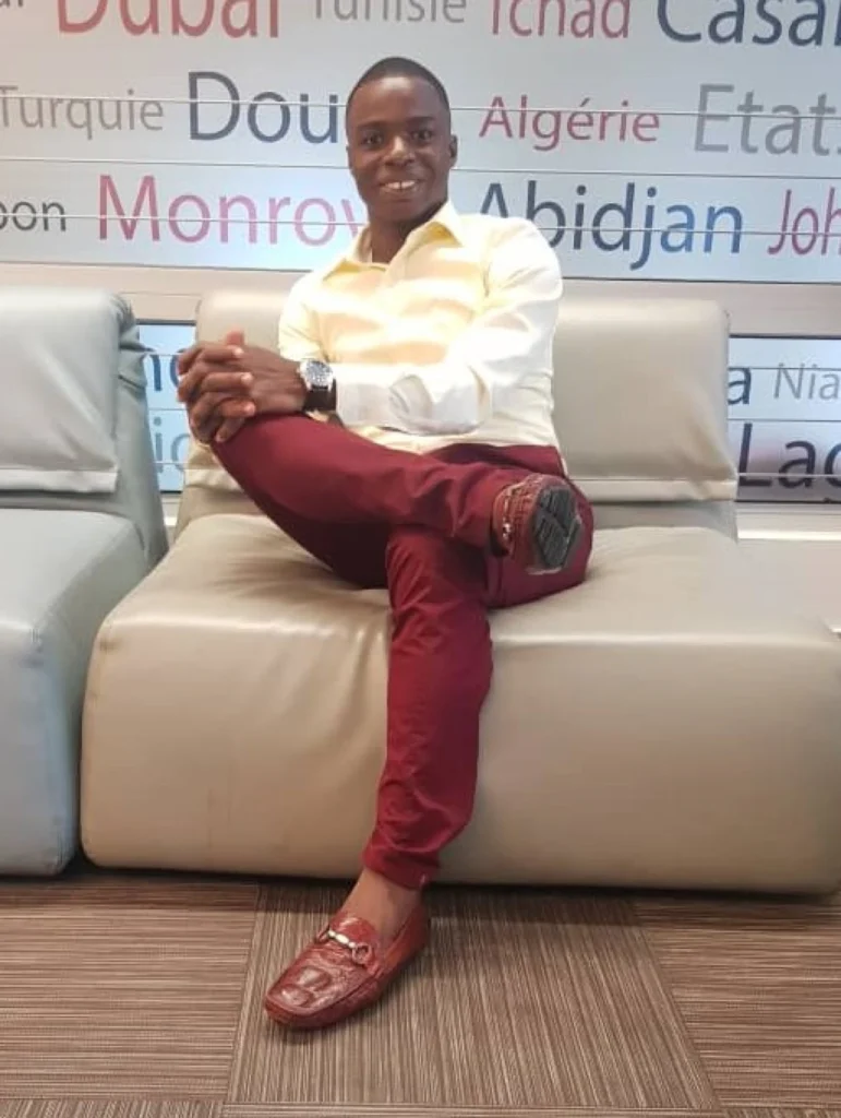 Houffoue Yao Hyacinthe sitting on a couch smiling in a yellow shirt and red pants