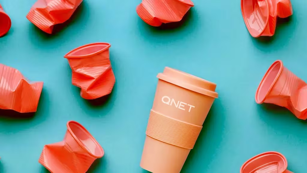 Championing Sustainability And Building A Green Legacy With Qnet 12 Orange reusable QNET tumbler surrounded by crumpled plastic cups