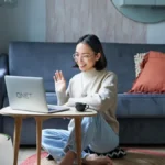 Girl who is doing QNET Part-Time talks to a business prospect on her laptop; she is wearing an Amezcua Chi Pendant and her home is equipped with HomePure Zayn