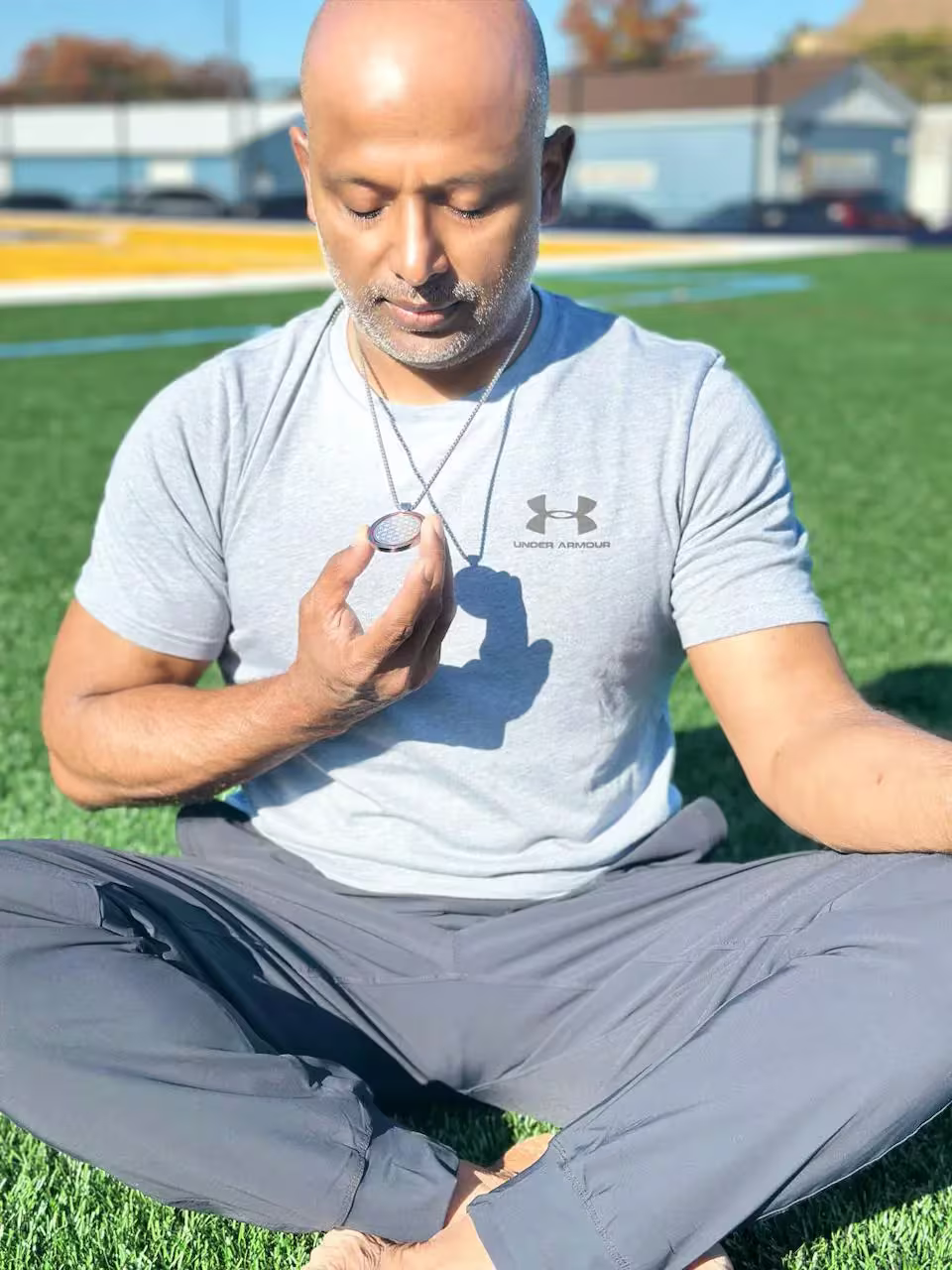 Breaking Boundaries With Qnet And Amezcua: How Anup Debnath Set A Guinness World Record At 51 2 Anup Debnath sitting on the grass while looking at the Amezcua wellness product, Chi Pendant 4, around his neck
