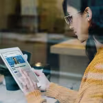 Caucasian girl engaging in hybrid learning with qLearn's management and leadership audio library on her tablet while she's at a cafe