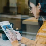 Caucasian girl engaging in hybrid learning with qLearn's management and leadership audio library on her tablet while she's at a cafe