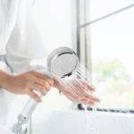 Hand holding a HomePure Rayn shower head with flowing water